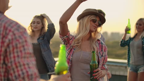 A-young-blonde-in-glasses-and-a-hat-moves-in-a-dance-with-her-friends-on-the-roof.-They-celebrate-a-rooftop-party